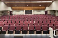 Back of room view of student auditorium seating, A/V booth center, and exit doors at rear of room