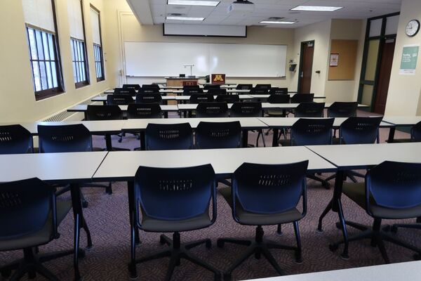 Front of room view with lectern on left in front of markerboard and projection screen partially raised, exit door on the right