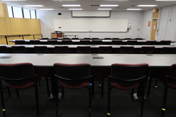 Front of room view with lectern on left in front of markerboard and projection screen partially raised, exit door on the right