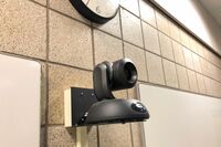 Camera mounted to a wall and instructor enabled adjustments to the lens to allow the instructor to be "seen" by the camera in more locations around the room