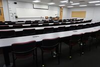 Front of room view with lectern on right in front of markerboard and projection screen partially raised, exit doors to left and right