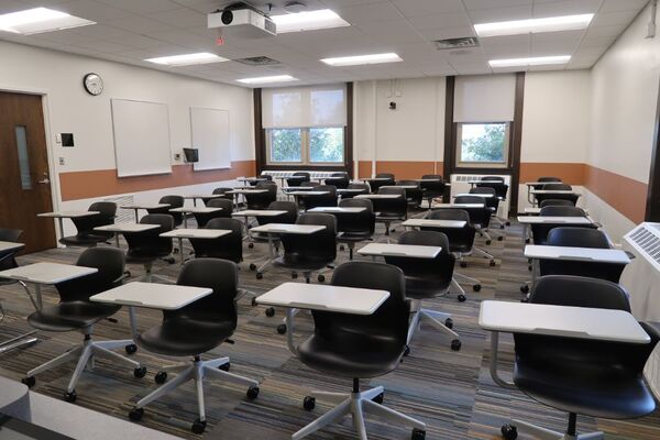 Back of room view of student tablet arm seating, side markerboards on left wall, and exit door center left of room