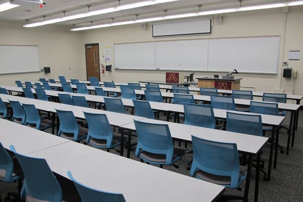 Front of room view with lectern on right in front of markerboard and projection screen partially raised