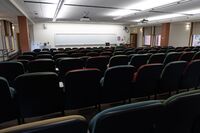 Front of room view with lectern on right in front of markerboard and exit doors front left and right