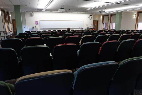 Front of room view with lectern on right in front of markerboard and exit doors on left and right