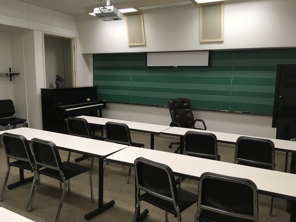 Photo of front of room from back of room with music staff chalkboard and piano.