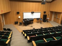 Photo of front of room from back of room with auditorium seating and piano at front.