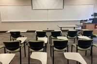 Front of room view with lectern on right in front of markerboard and projection screen partially raised