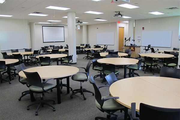 View of room with lectern center in front of markerboards and projection screen on the left wall