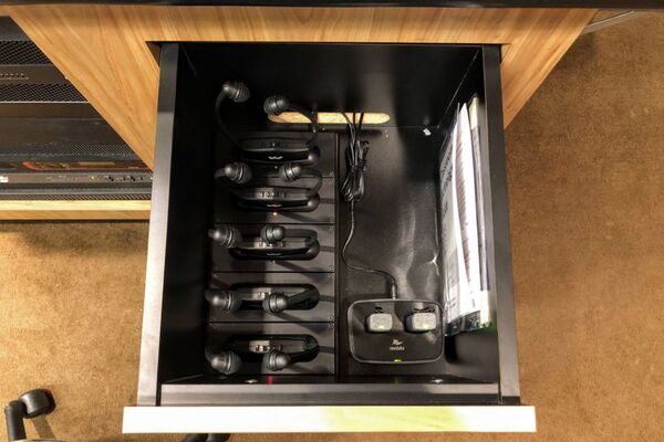 Pedestal - inside view of drawer showing two wireless mics in charging base and assistive listening devices in charger