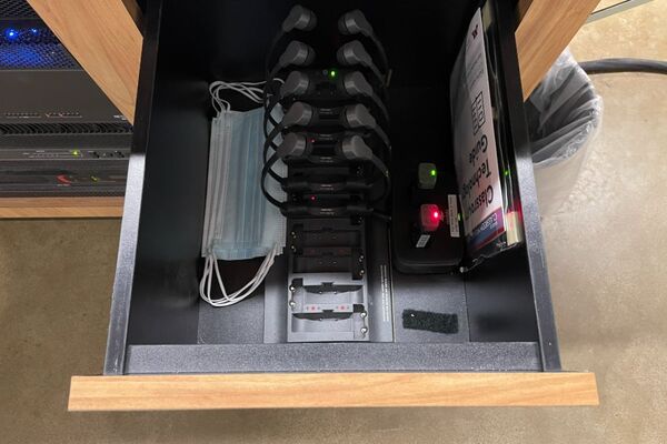 Pedestal - inside view of drawer showing two wireless mics in charging base and assistive listening devices in charger