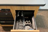 Pedestal - inside view of drawer showing two wireless mics in charging base and assistive listening devices in charger