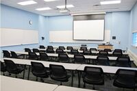 Front of room view with lectern on right in front of markerboard and projection screen lowered