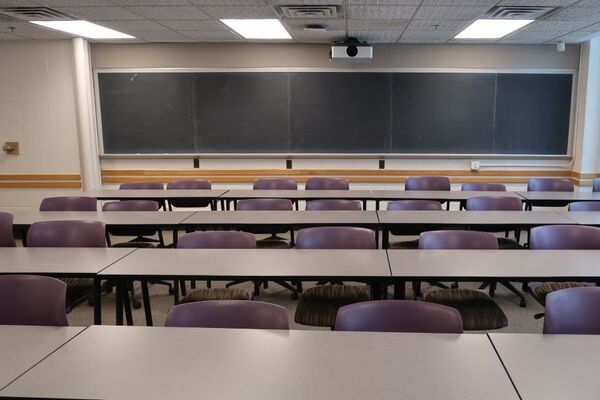 Back of room view of student table and chair seating and chalkboard on back wall