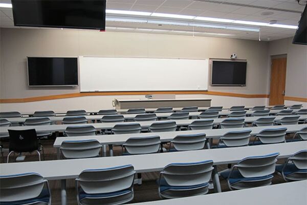 Front of room view with lectern center in front of markerboard and display screens to left and right