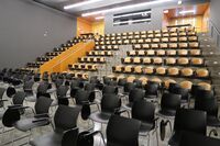 Back of room view of student tablet arm (front) and auditorium seating (rear) and double exit doors at rear of room