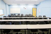 Back of room view of student table and chair seating and exit door at right rear of room