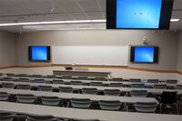 Front of room view with lectern center in front of markerboard and display screens to left and right