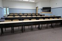 Back of room view of student tiered table and chair seating and display monitor on right rear wall