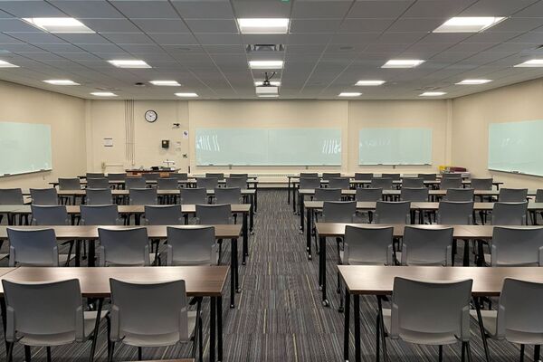 Front of room view with lectern on left in front of markerboard, table and chair seating