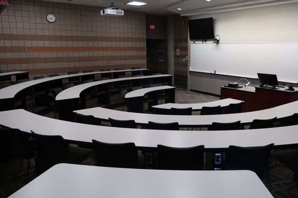 Front of room view with lectern on center in front of markerboard and display screen on the upper left