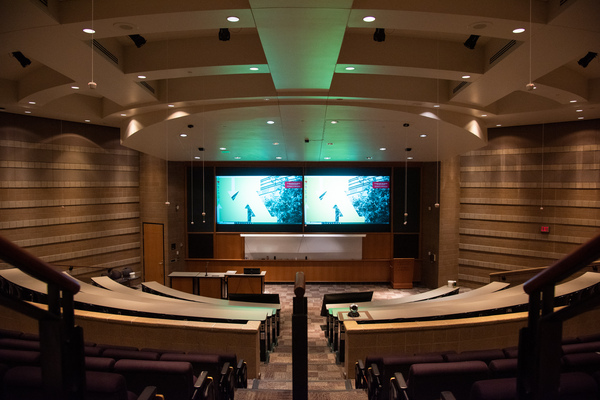 Audience view from rear center of room.  Both projectors and the entire white board visible in the front center.  Student mics and room camera are also visible.  