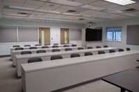 Back of room view of student table and chair seating and confidence monitor at right rear of room