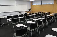 Front of room view with lectern on right in front of markerboard and projection screen partially raised