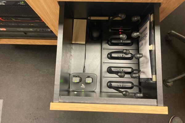 Pedestal - inside view of drawer showing two wireless mics in charging base and assistive listening devices in charger