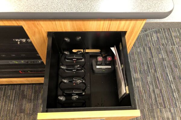 Pedestal - inside view of drawer showing two wireless mics in charging base and assistive listening devices in charger