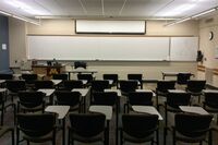 Front of room view with lectern on left in front of markerboard and projection screen partially raised