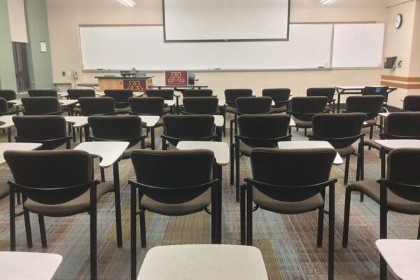 Front of room view with lectern on left in front of markerboard and projection screen partially raised, exit door on right wall near front of room