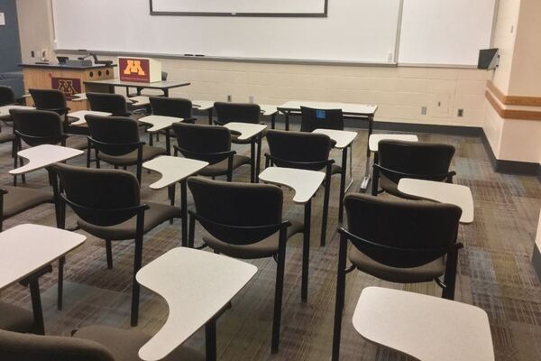 Front of room view with lectern center in front of markerboard and projection screen partially raised, exit door on right wall