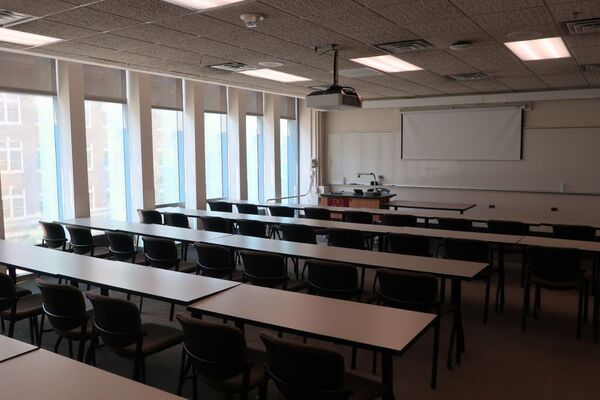 Front of room view with lectern on left in front of markerboard and projection screen partially raised