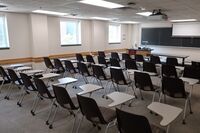 Front of room view with lectern on left in front of chalkboard and projection screen partially raised