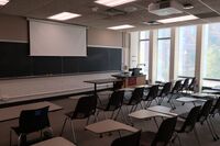 Front of room view with lectern on right in front of chalkboard and projection screen partially raised