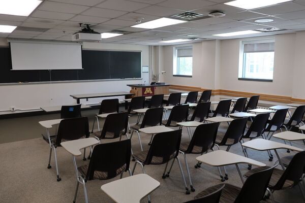 Front of room view with lectern on left in front of chalkboard and projection screen partially raised