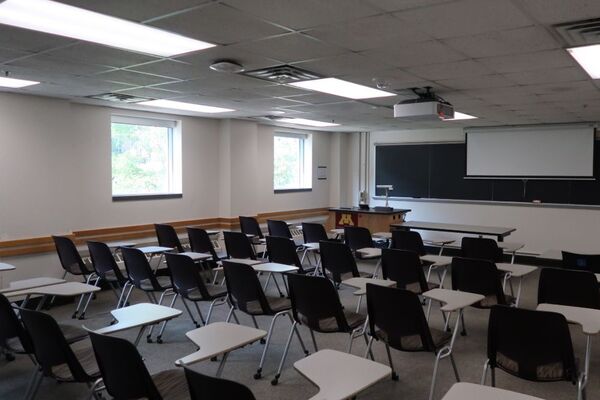 Front of room view with lectern on left in front of chalkboard and projection screen partially raised