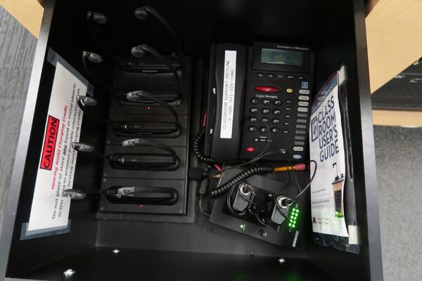 Pedestal - inside view of drawer showing two wireless mics in charging base, assistive listening devices in charger, and telephone